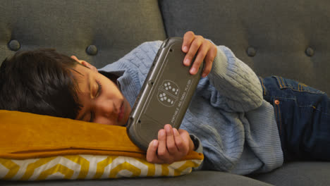 Young-Boy-Lying-On-Sofa-At-Home-Playing-Game-Or-Streaming-Onto-Handheld-Gaming-Device-3